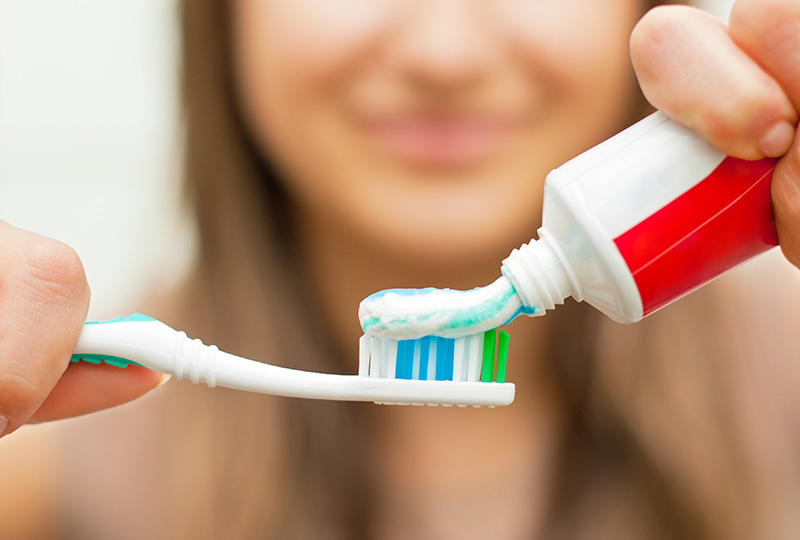 A person s hand is holding a tube of toothpaste, with the cap off and the toothbrush partially inserted into it.